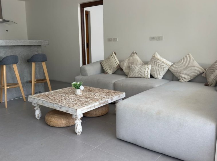 Pièce de vie canapé gris table sculptée blanche bar tabourets appartement Koh Samui