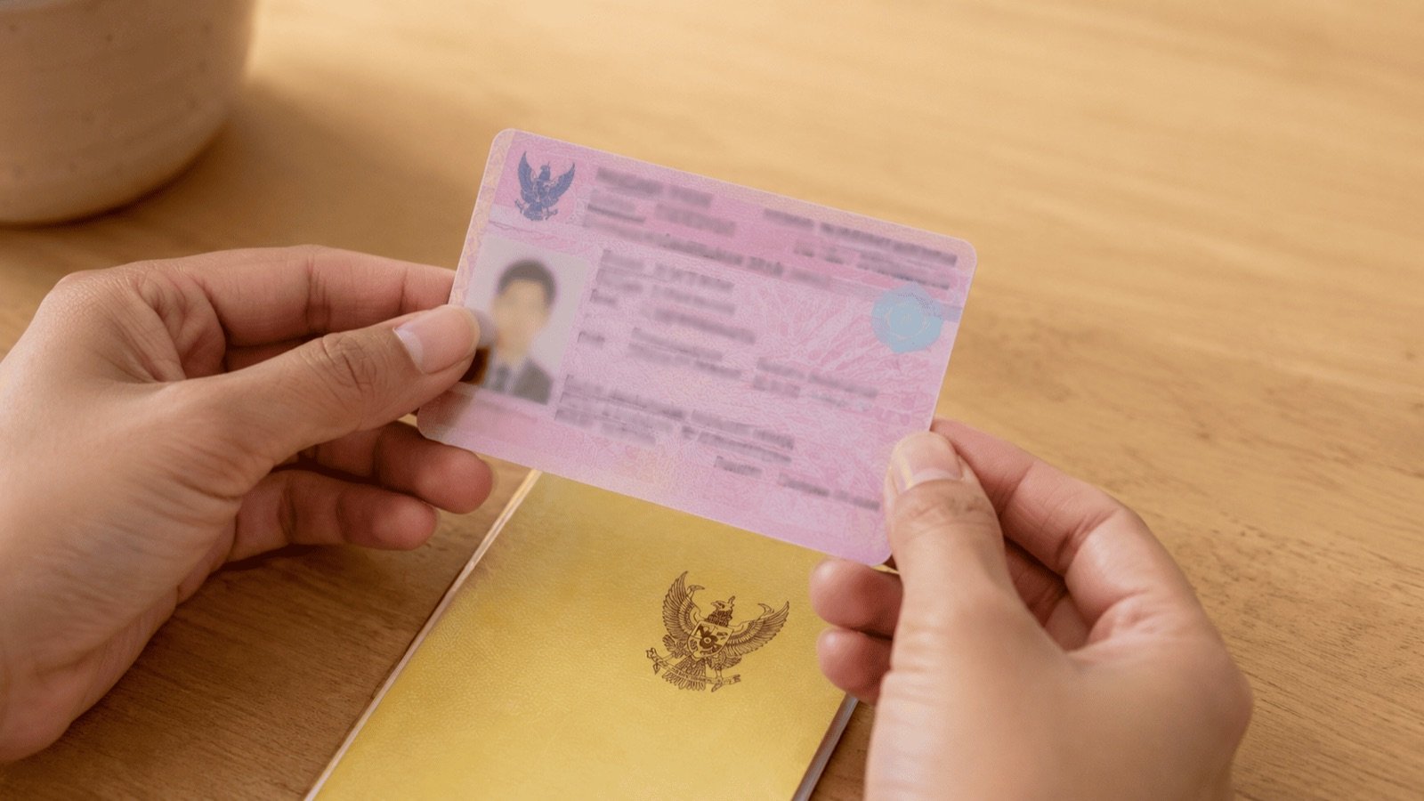 Carte d'identité rose pour étranger tenue au-dessus d'un livret jaune de maison en Thaïlande