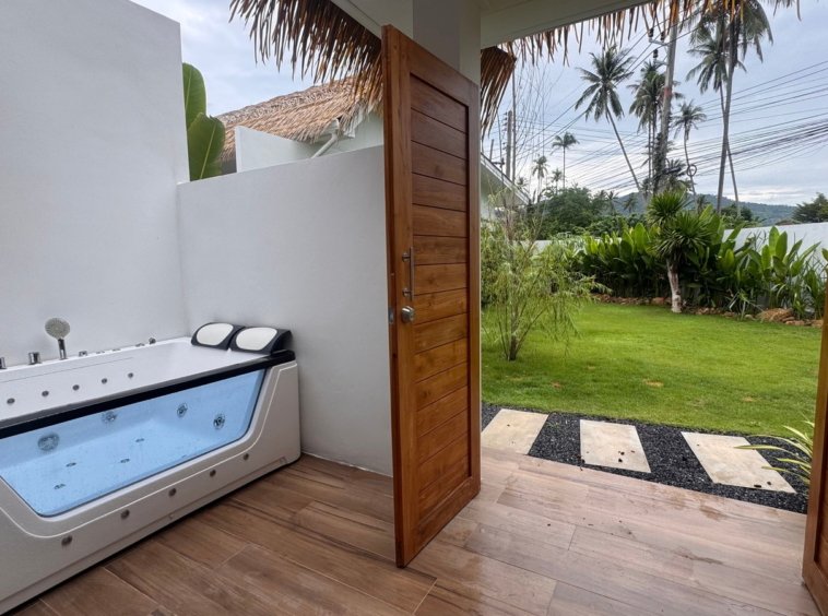 Terrasse avec baignoire balnéo ouverte sur le jardin et les cocotiers
